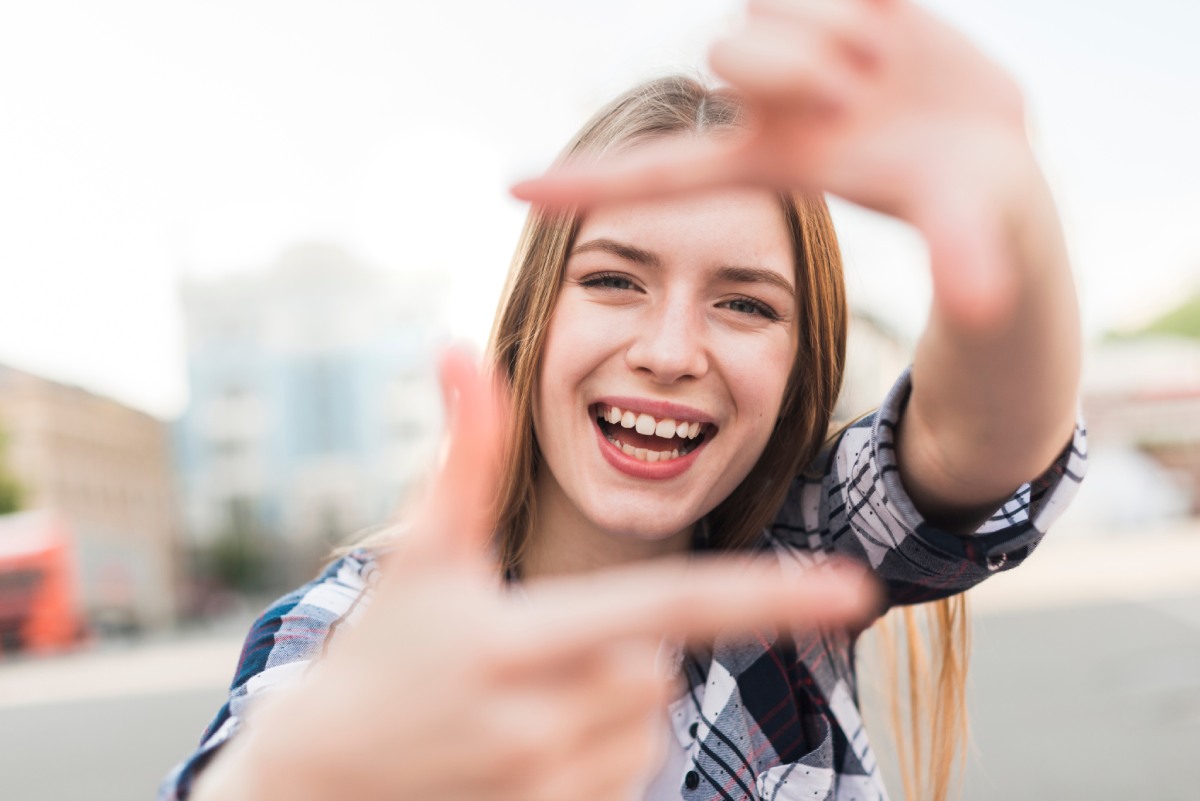 A smiling woman holding up her hands in the shape of a square.