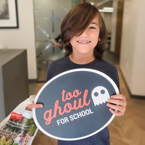 A happy patient holding a sign saying, "too ghoul for school."