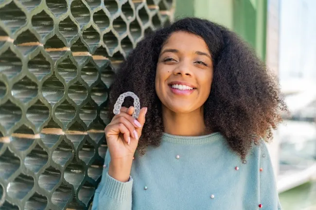 A woman holding up her Invisalign aligner.